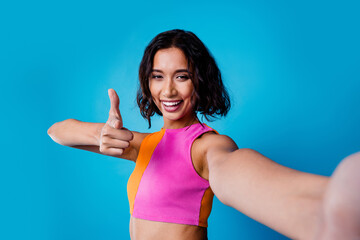 Young stylish woman gestures confidently with a thumbs up against vibrant blue background,...