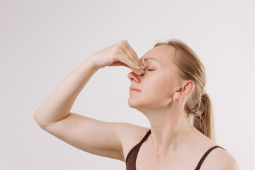 Woman with light brown hair holding her nose, expressing discomfort due to a runny nose, in a...