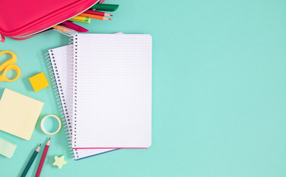 Back to school. A pencil case with pencils and pens, various office supplies, as well as an eraser, scissors and an open notebook on a light green background. Flat lay, top view