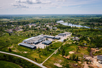 Aerial view of a rural industrial zone near a small town and lake, with warehouse buildings, roads, fields, and surrounding residential areas..