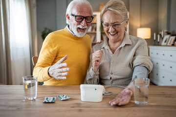 Happy senior couple measuring blood pressure at home
