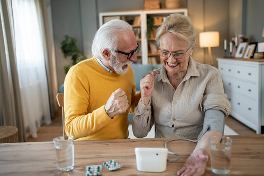 Happy senior couple checking blood pressure at home