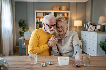Senior couple monitoring blood pressure at home using digital device