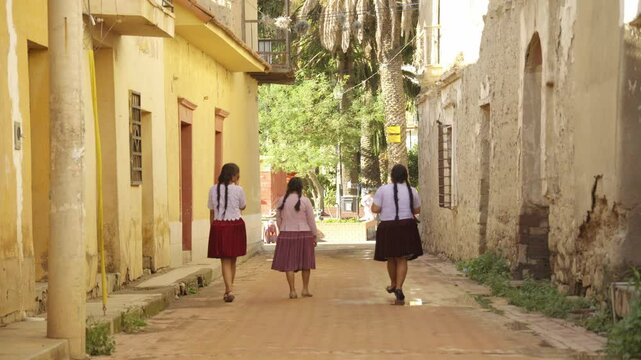 Three indigenous women walking and talking on a street in a valley in Bolivia.