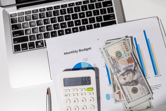 A monthly budget graph paper is placed on the desk alongside a calculator, laptop, and cash—creating a complete setup for personal finance management, bill tracking, and financial goal-setting.

