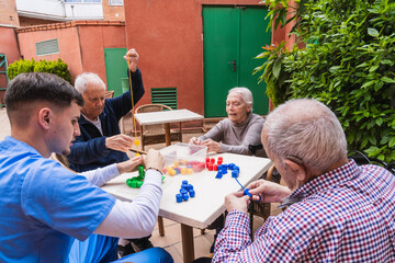 Nurse assisting elderly people playing with colorful construction toys at an outdoor nursing home,...