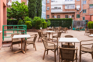 Wicker chairs and white tables standing on tiled patio in tranquil garden of nursing home, offering peaceful outdoor space