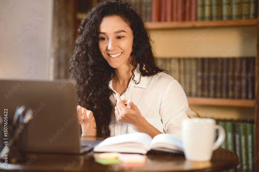 Poster online video call and communication. portrait of smiling curly woman sitting at table, using laptop 