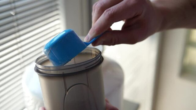 Close up of a man preparing protein shake. Pouring chocolate protein powder in a shaker