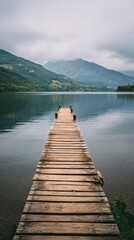 Tranquil Wooden Dock Extends Over Calm Lake Surrounded by Mountains on a Cloudy Day