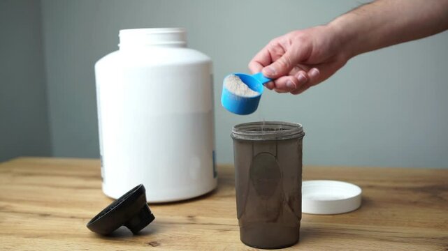 Close up of a man preparing protein shake. Pouring chocolate protein powder in a shaker