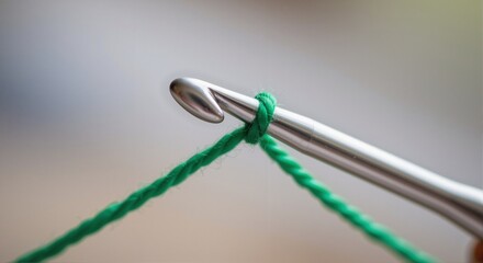 Close-up of aluminum crochet hook with green yarn in soft focus background