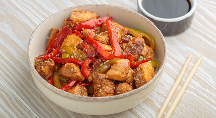 Chicken stir fry with red and green bell peppers sprinkled with sesame seeds, served in bowl, with chopsticks and soy sauce aside, composing a delicious asian meal