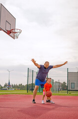 A father stands in a defensive position playing basketball with his little daughter. Father's Day.