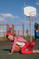 Funny funky girl in a baseball cap playing with a basketball on the playground