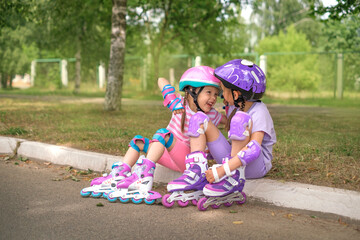 Laughing humorous sisters put on laughing while sitting on the side of the road relaxing after roller skating