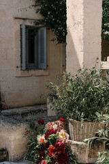 window with flowers in provence. Wicker basket with olive tree branches, peony flowers, mediterranean town. Street aesthetic mediterranean decoration. Event or wedding decor. 