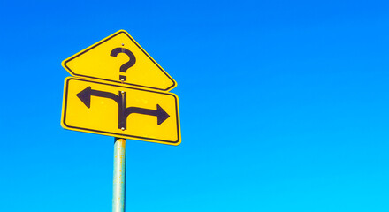 A yellow sign with a question mark and arrows pointing left and right against a blue sky outdoor view