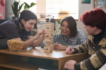 Smiling teenage girl playing board game with two friends at home or in school dorm and removing...