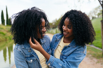 Two twin sisters are embracing and smiling outdoors, enjoying a special moment together in a park setting