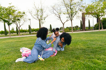 Two twin sisters enjoying a sunny day at the park, playing joyfully with their niece on a blanket...