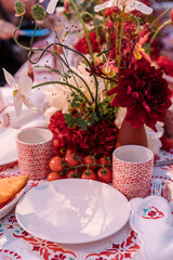 table setting for a wedding with red flowers, tomatoes and traditional countryside crockery