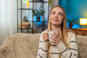 Caucasian woman girl sitting at home sofa holding hot tea cup relaxing enjoying quiet moment. Warm...