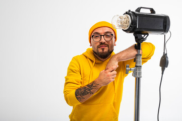 Portrait of a young man in yellow hoodie and beanie posing with a studio light against white...