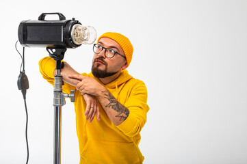 Portrait of a young man in yellow hoodie and beanie posing with a studio light against white...