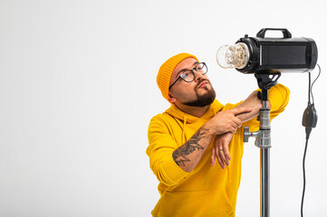 Portrait of a young man in yellow hoodie and beanie posing with a studio light against white...