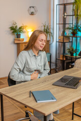 Disappointed Caucasian female freelancer feeling overeating during work process on laptop in home...