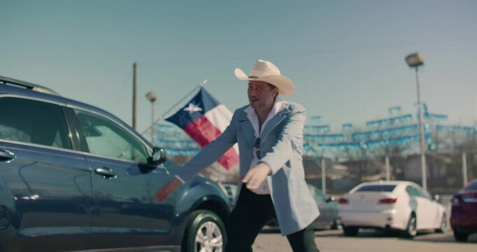Car Salesman Wearing Cowboy Hat Showing Off Cars At Car Dealership