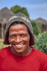 village rural ,portrait of african man , in front of a house with thatched roof , countryside living, he is wearing a beanie with motifs