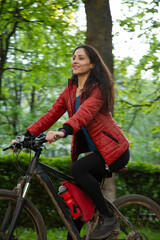 Beauty smiling woman in sport black cap biking on bicycle on spring trees background. Sporty wear...
