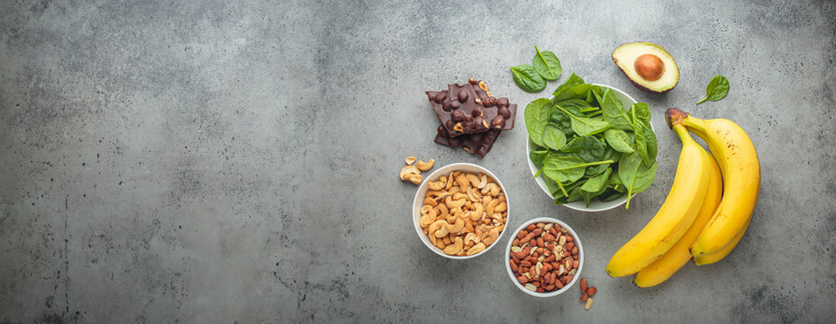 Assorted magnesium rich foods like bananas, spinach, peanuts, cashews, and dark chocolate on a gray background, mineral for mood and brain boost