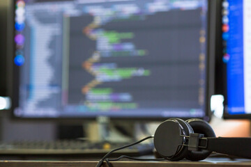 Headphones on desk with blurred code on monitor