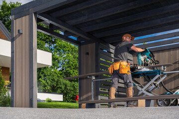 Skilled Carpenter Works on a Wooden Carport Cover in a Sunny Outdoor Setting With Greenery Nearby