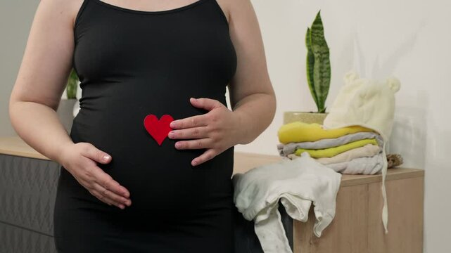 Pregnant woman holding red heart shape and feel love for unborn baby in belly. Awaiting for baby. Concept of maternity and pregnancy care