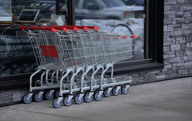 five empty shopping carts put together outside of grocery store stainless steel or metal with wheels and red handles stacked together outside of grocery store window horizontal format room for type 