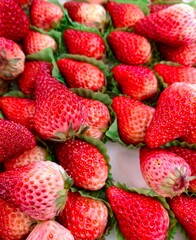 bright red and ripe strawberries are arranged attractively on green leaves, showcasing their freshness bustling market on sunny afternoon. close-up.