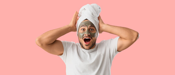 Handsome young shocked man with cosmetic clay mask on face against pink background
