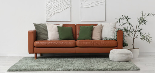 Brown leather sofa with soft pillows and pouf near white wall in living room
