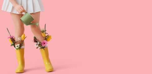 Young woman in gumboots with beautiful flowers holding watering can on pink background with space for text © Pixel-Shot