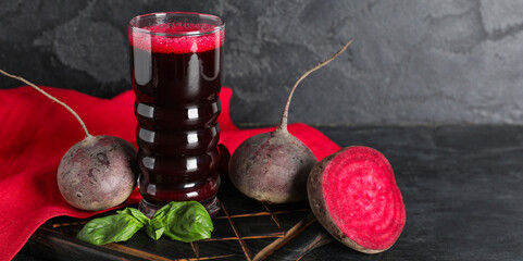 Glass of fresh beet juice with basil and vegetables on black background