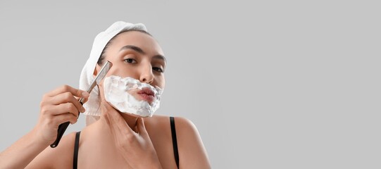 Beautiful young woman shaving her face on grey background with space for text