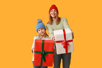 Cute little girl and her mother with Christmas gift boxes on yellow background