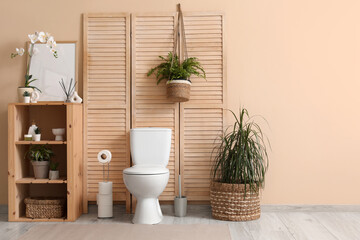 Modern interior of restroom with ceramic toilet bowl, shelving unit and plants