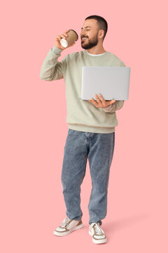 Fototapeta Young man with laptop and cup of coffee on pink background