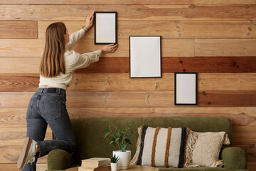 Woman hanging blank photo frame on wooden wall at home