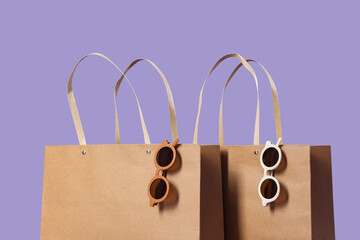 Paper shopping bags with stylish sunglasses on lilac background